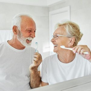 couple brushing their teeth in front of a mirror 