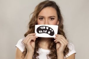 woman holding picture of frowning, unhealthy mouth in front of her smile